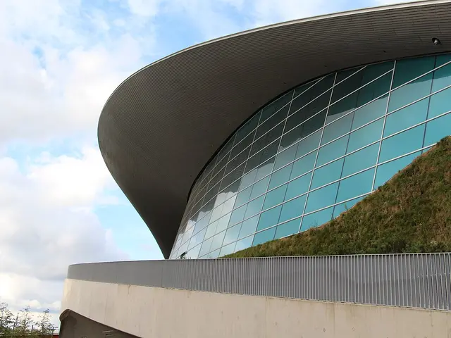 The curved glass and roof exterior of a modern aquatics centre building, with no people visible.