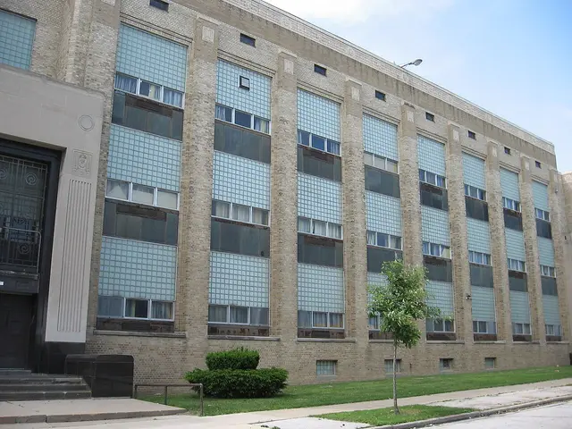 The brick exterior of a large multi-storey high school building with tall glass-block windows.