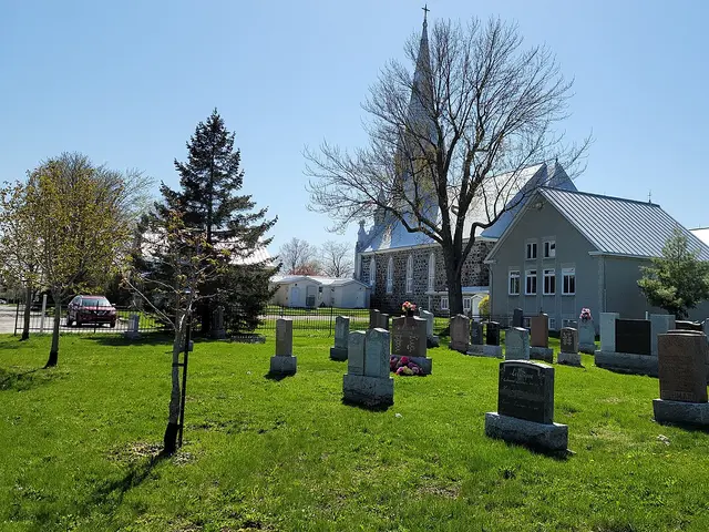 A white steepled Catholic church seen past a cemetery in Saint-Hubert, Quebec