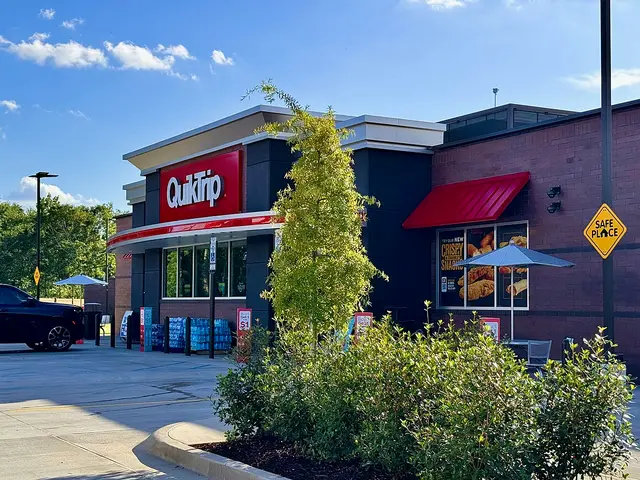 The exterior of a QuikTrip convenience store and gas station with a red and dark storefront and outdoor seating