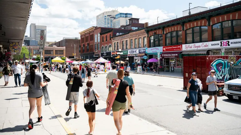 Des gens qui marchent le long d'une rue ensoleillée bordée d'immeubles en briques près du Marché By d'Ottawa